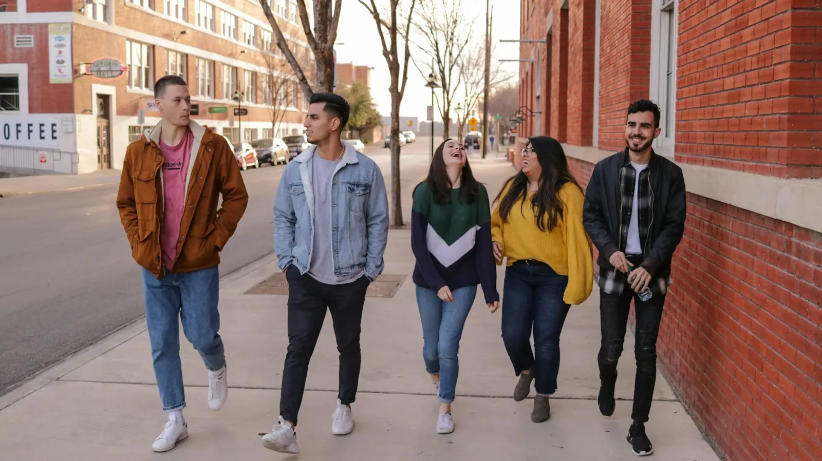 Five friends laughing as they walk down a city sidewalk together